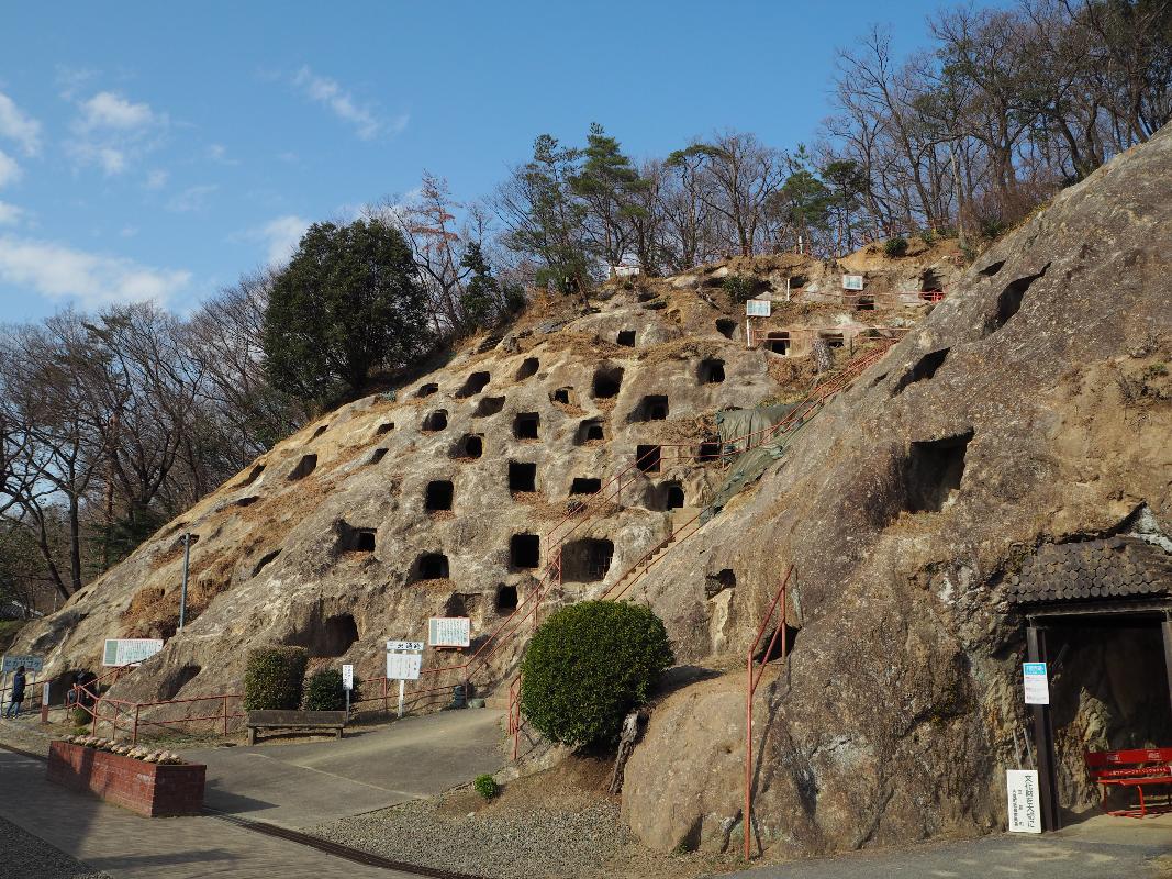 岩山の斜面に多数の穴が空いており、岩山の上には木々が生えている遺跡「吉見百穴」の画像